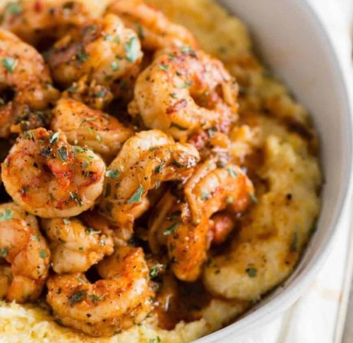 A bowl of creamy grits topped with seasoned shrimp and garnished with herbs.