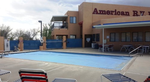 A pool area with a covered pool, lounge chairs, and a building labeled "American R.V. Park" in the background.