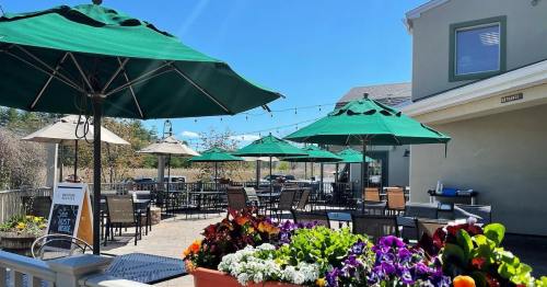 Outdoor patio with green umbrellas, tables, and colorful flowers under a clear blue sky.