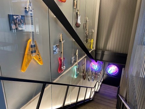 A staircase with a glass wall displaying various guitars and framed photos, illuminated by colorful neon lights.