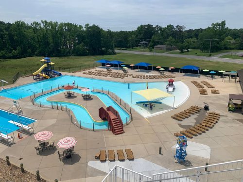 Aerial view of a swimming pool area with slides, lounge chairs, and shaded seating under colorful umbrellas.