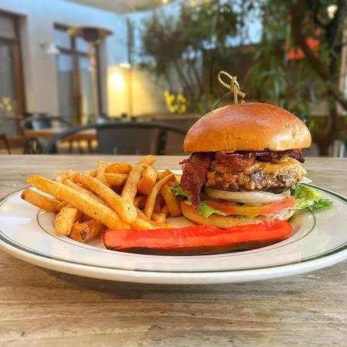 A juicy burger topped with bacon, lettuce, and tomato, served with crispy fries and a slice of red pepper on a plate.