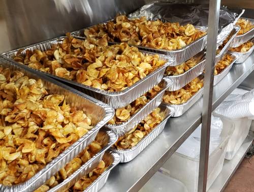 A row of aluminum trays filled with golden-brown potato chips stacked on a metal shelf.