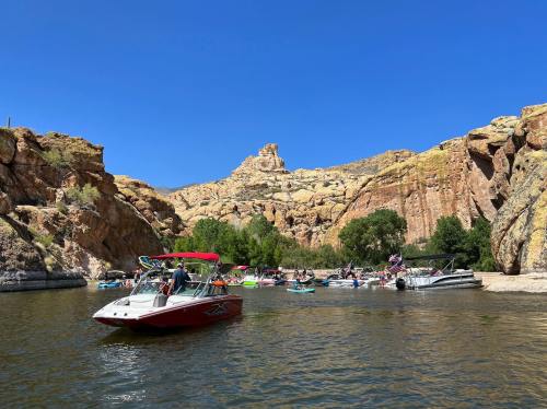 Boats and kayaks on a calm river surrounded by rocky cliffs and greenery under a clear blue sky.