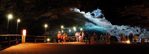 Visitors explore a dimly lit cave, illuminated by lights, with rocky formations and a wooden walkway.