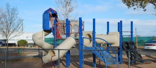 A colorful playground with a slide, climbing structures, and a fence, set against a clear sky.