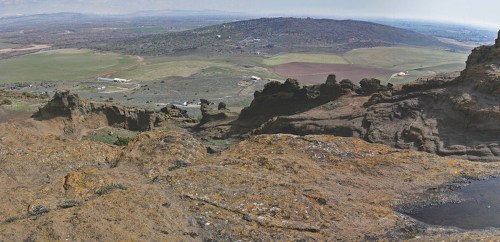 A panoramic view of rocky terrain and rolling green hills under a clear sky.