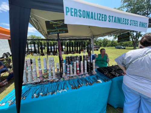 A vendor booth displaying personalized stainless steel rings, bracelets, and necklaces at an outdoor market.