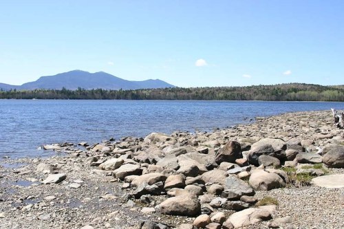 A serene lakeside view with rocky shorelines and distant mountains under a clear blue sky.