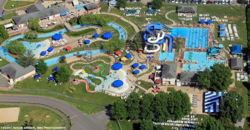 Aerial view of a vibrant water park featuring pools, slides, and lounging areas with umbrellas and greenery.