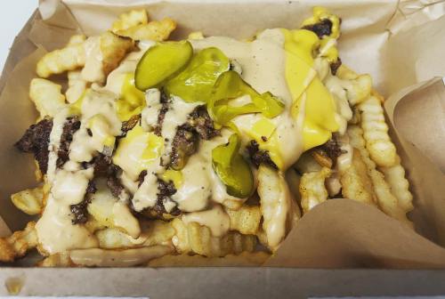 A box of crinkle-cut fries topped with cheese sauce, pickles, and seasoned ground beef.