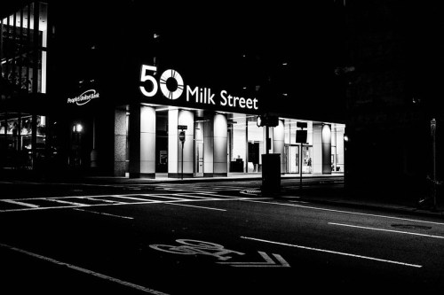 Nighttime view of 50 Milk Street building, illuminated signage, and empty street in black and white.