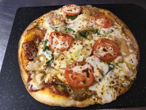 A freshly baked pizza topped with cheese, tomatoes, green peppers, and chicken on a black baking tray.