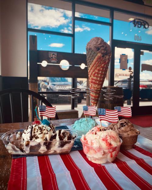 A variety of ice cream desserts on a table, with small American flags, set against a bright window view.