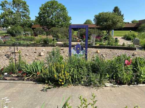 A vibrant garden with colorful flowers and a purple frame sculpture in the center, under a clear blue sky.