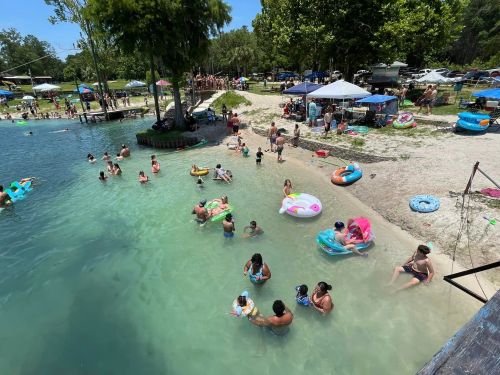 A lively beach scene with people swimming, floating on inflatables, and enjoying a sunny day by the water.