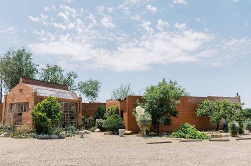 A rustic adobe building surrounded by greenery and trees under a clear blue sky.