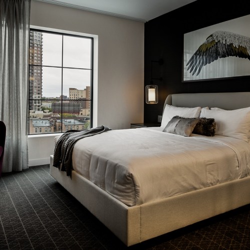 Modern hotel room with a large bed, stylish decor, and a window showcasing a city view.