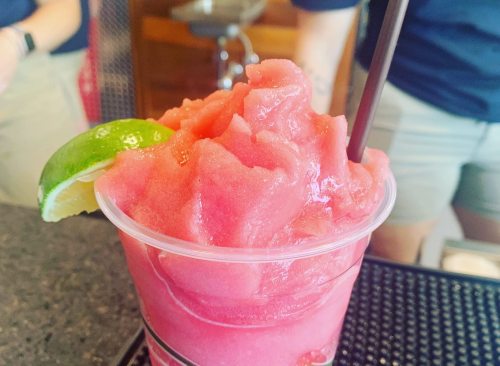 A refreshing pink slush drink in a clear cup, garnished with a lime wedge and a straw.