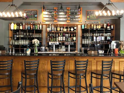 A wooden bar with high stools, shelves of liquor, and a chalkboard menu displaying featured drinks.