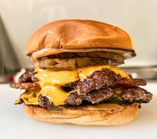 A delicious burger with two beef patties, melted cheese, bacon, and grilled onions on a toasted bun.