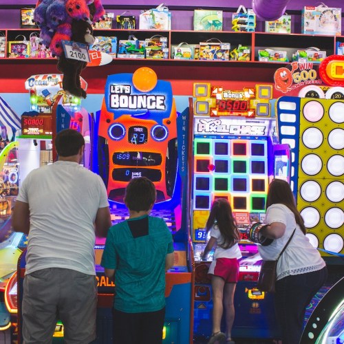 A family enjoys arcade games in a colorful entertainment center filled with various machines and toys.