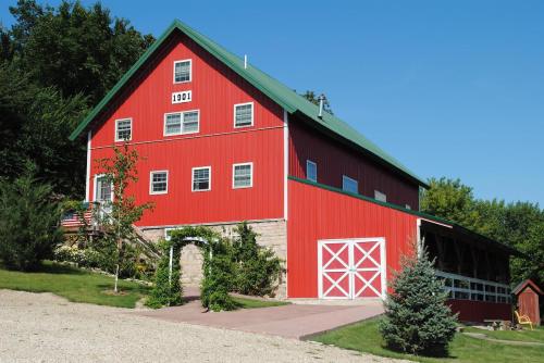 A red barn-style building with a green roof, surrounded by greenery and a gravel path under a clear blue sky.
