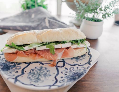 A fresh sandwich with prosciutto, cheese, and arugula on a decorative plate, set on a wooden table.
