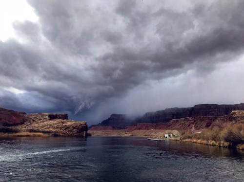 A river flows through a canyon under a dramatic sky filled with dark clouds, hinting at an approaching storm.