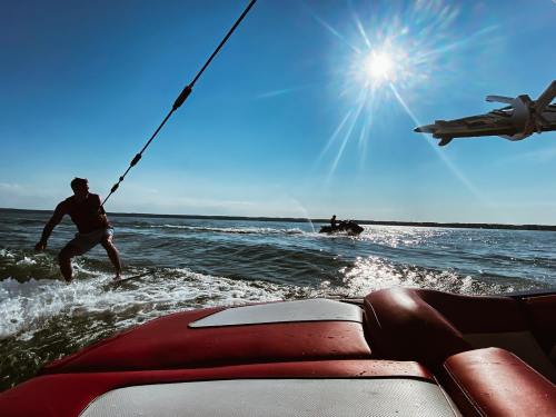 A person water skiing behind a boat on a sunny day, with another person on a jet ski in the background.
