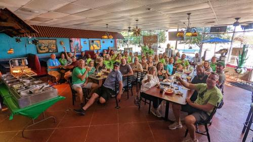 A large group of people in matching green shirts gathered in a restaurant, smiling and enjoying a meal together.