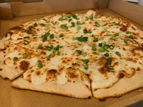 A freshly baked cheese pizza with green onions, served in a cardboard box.