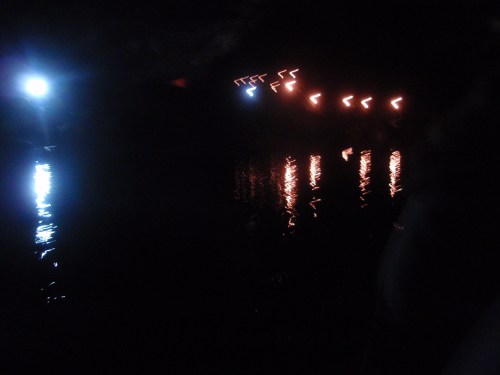 A dark scene with reflections on water, featuring blue and orange lights in a zigzag pattern against a night sky.