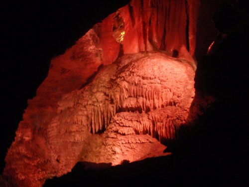 A dimly lit cave wall with striking red lighting, showcasing unique rock formations and stalactites.