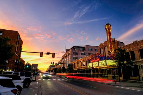 A vibrant sunset over a city street, featuring a historic theater marquee and light trails from passing cars.