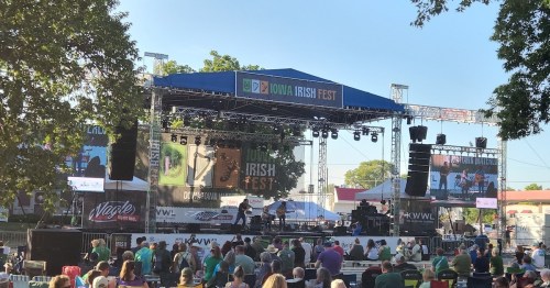 A lively outdoor stage at Iowa Irish Fest, with musicians performing and an audience in green attire enjoying the event.
