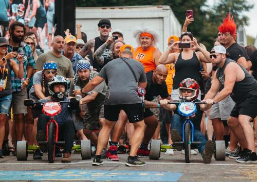 Two racers on tricycles are about to start a race, surrounded by an enthusiastic crowd cheering them on.