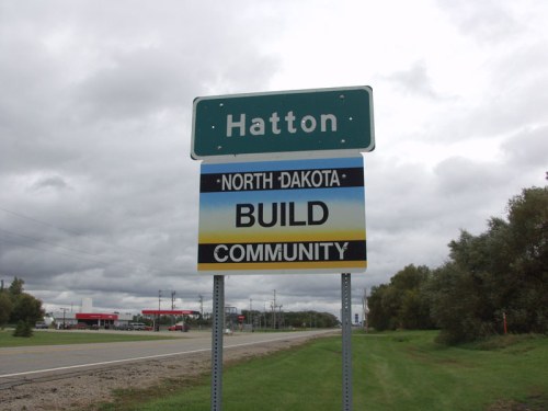 Sign for Hatton, North Dakota, with a message to "Build Community" against a cloudy sky backdrop.
