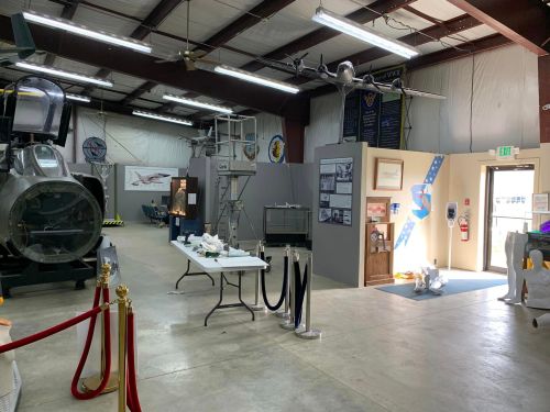 Interior of a museum featuring aircraft displays, informational panels, and a reception area with seating.