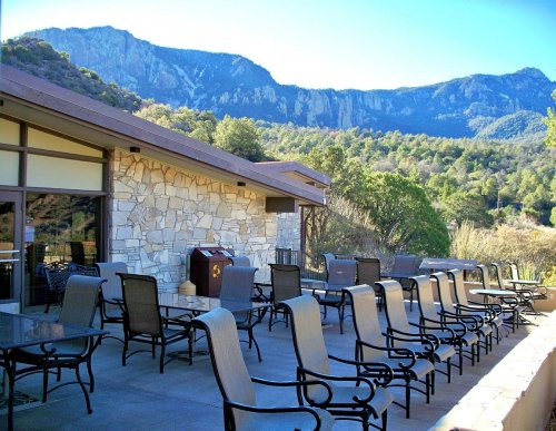 A patio with metal chairs and tables overlooks a mountainous landscape under a clear blue sky.