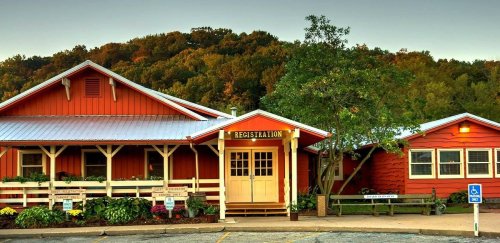 A charming red building with a registration sign, surrounded by greenery and hills in the background.