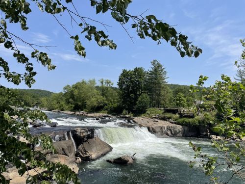 A scenic view of a river with cascading waterfalls, surrounded by lush greenery and a clear blue sky.
