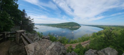 A panoramic view of a river winding through lush green hills under a blue sky with scattered clouds.