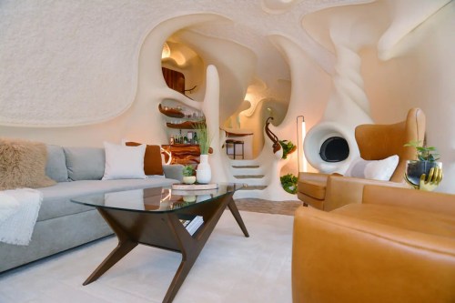 A modern, organic-shaped living room with curved walls, a glass coffee table, and stylish furniture in warm tones.