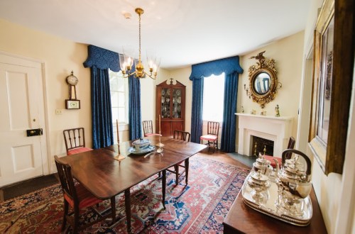 A cozy dining room with a wooden table, chairs, blue curtains, a china cabinet, and decorative accents.