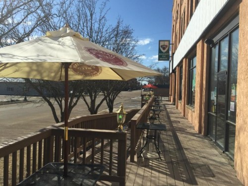 A sunny outdoor patio with umbrellas and tables, next to a building, on a clear day.