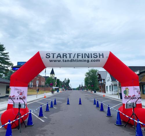 Red inflatable archway labeled "START/FINISH" on a street, with blue cones and banners for a race event.