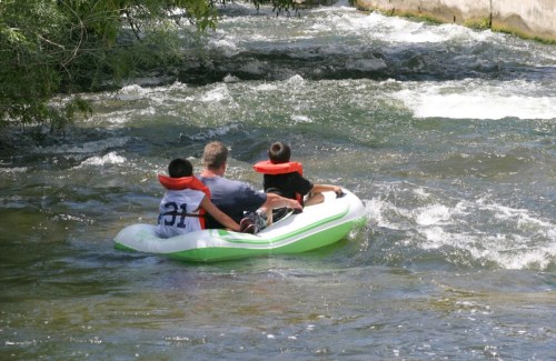 A man and two children in life jackets float down a river in a small inflatable boat.