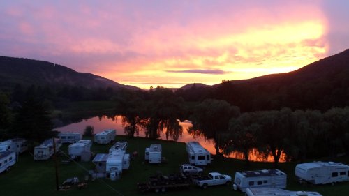 A serene sunset over a lake, with RVs parked nearby and mountains in the background.
