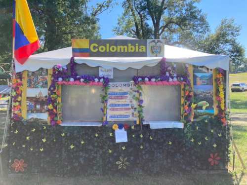 A colorful booth decorated with flowers and flags, labeled "Colombia," showcasing cultural information and images.